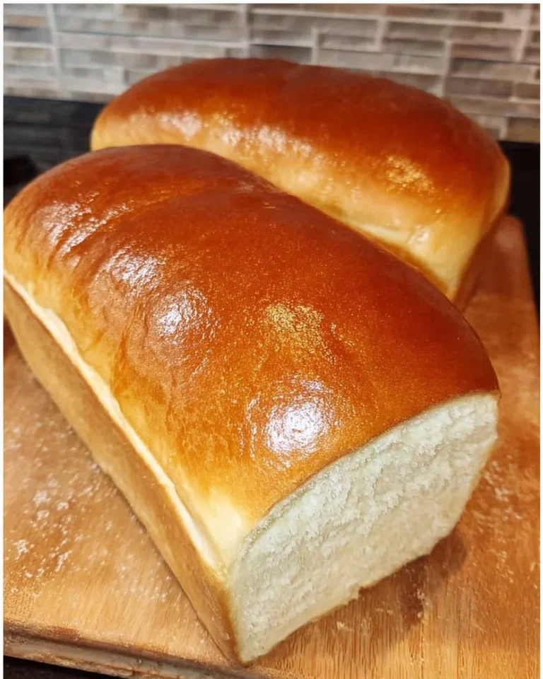 Loaf of Amish White Bread freshly baked and sliced on a wooden cutting board.